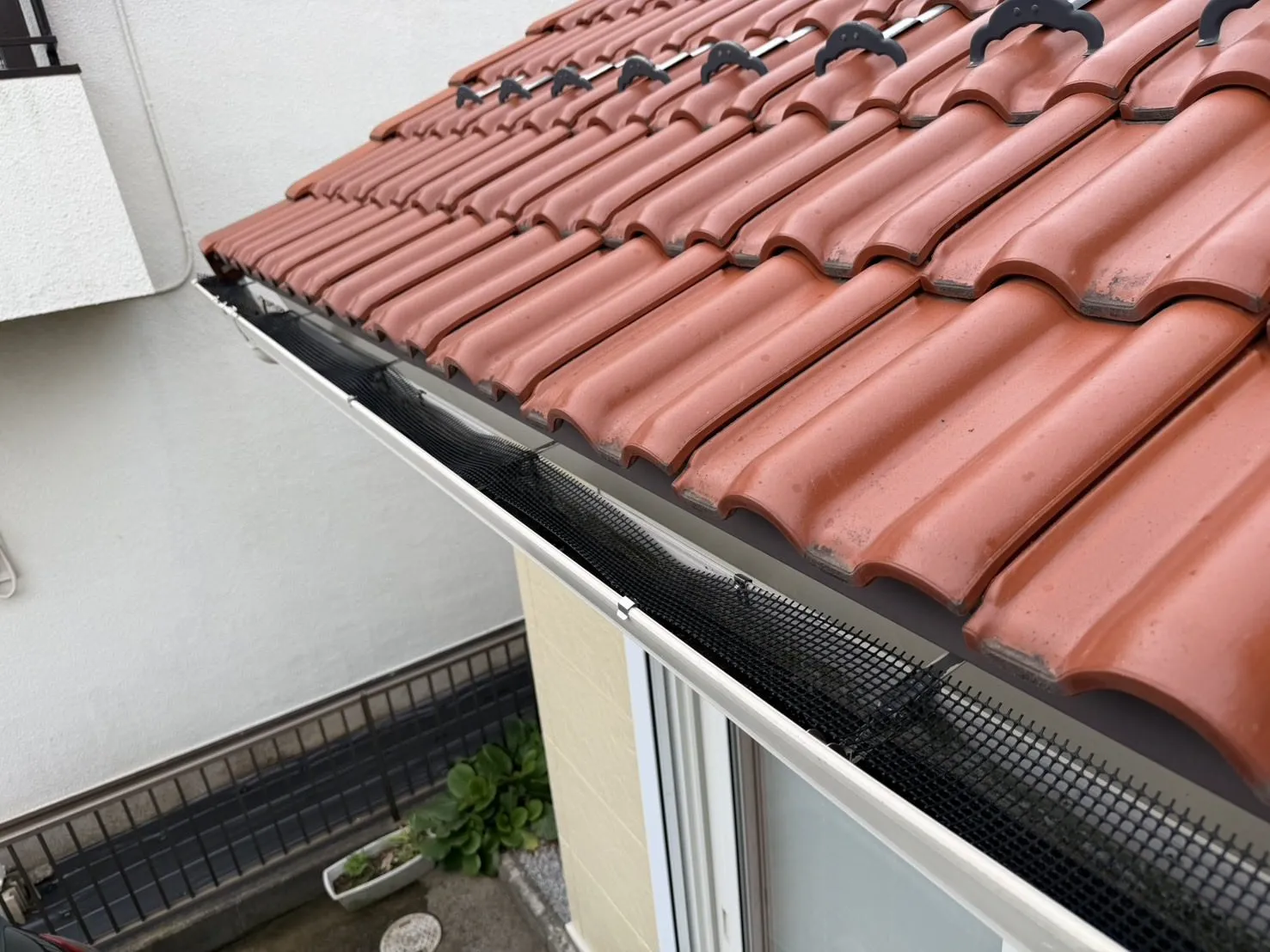 瓦屋根の軒先に沿って、雨樋の上にかぶせられた落ち葉よけネット